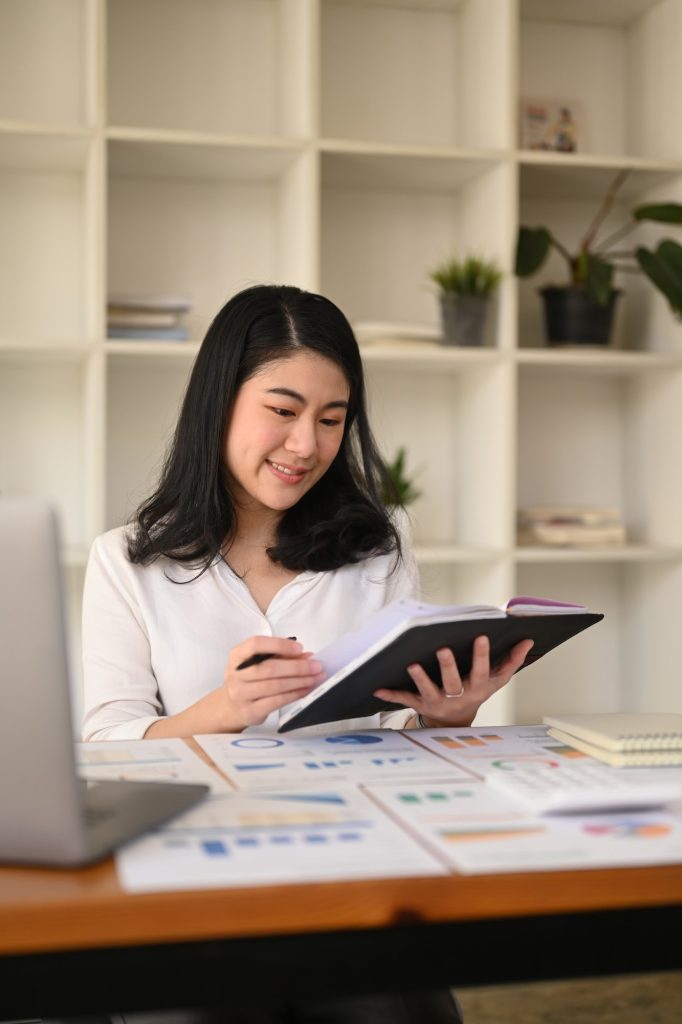 Attractive young businesswoman working with laptop and document at corporate office.