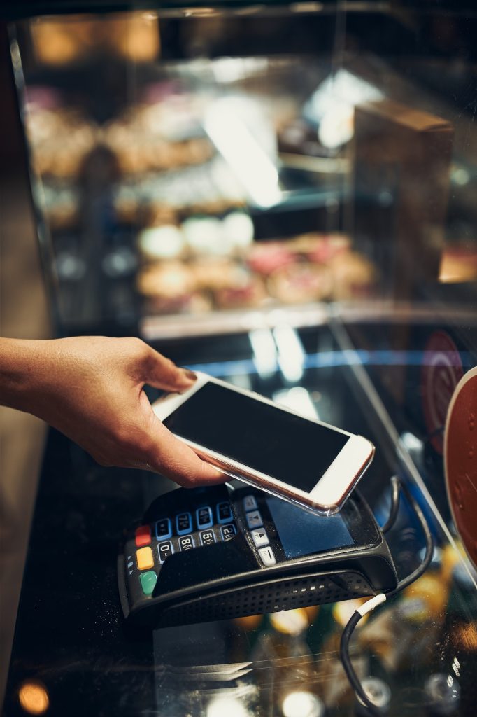 Woman paying in coffee shop using contactless method of payment via mobile phone